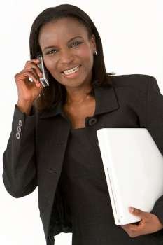 An African American businesswoman walking with a laptop under arm and chatting on her mobile phone