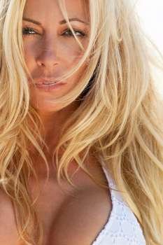Close up sensual portrait of a beautiful blond woman, shot outside in natural light wearing a white bikini with the focus on her eye.