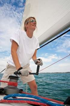 Shot of beautiful young woman on the deck of a boat operating a winch to hoist a sail