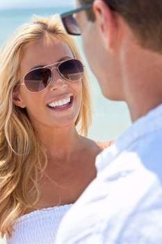 A sexy and attractive man and woman couple wearing sunglasses and having romantic fun laughing in the sunshine at the beach