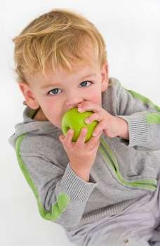 A young blue eyed blond boy eating a green apple