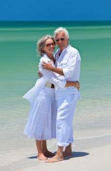 Romantic and happy senior man and woman couple dressed in white and embracing on a deserted tropical beach with bright clear blue sky