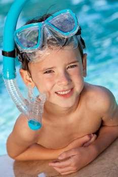 A happy young boy child relaxing on the side of a swimming pool wearing blue goggles and snorkel