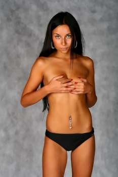 Studio shoot of a young girl in panties shirtless. Covers breasts with hands.