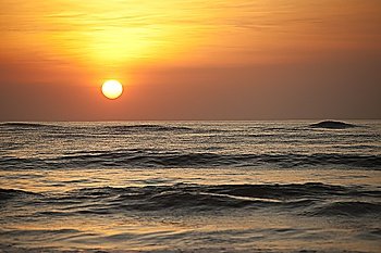 Sun setting over the calm ocean with an orange glow