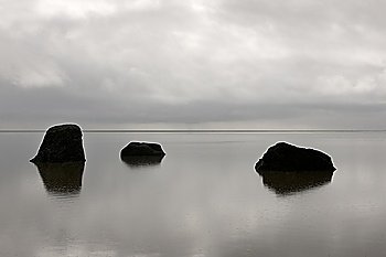 Three solitary rocks rising from the calm ocean against the horizon on a cloudy day
