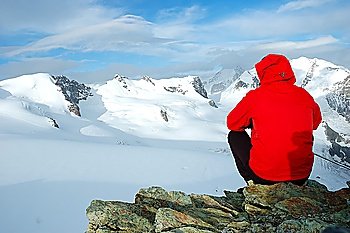 Mountaineer sitting on a stone looking at big glacier and snowed mountain. West Alps, Italy.