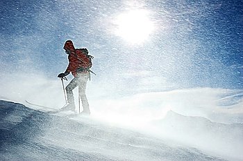 A lonely backcountry skier reaching the summit of the mountain during a snowstorm, horizontal orientation