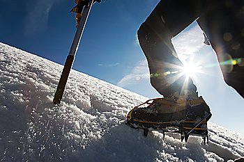 Mountain climber: detail on boot with ice crampon and ice axes; back-light