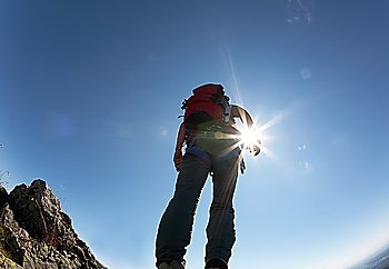 Climber, with climbing gears, standing on a stone at the top of his route, over a deep blue sky.