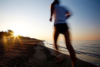 Young male runner running on a empty beach at dawn. Blur effect.