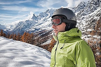 Portrait of young caucasian skier with ski goggles and helmet. on background a winter alpine landscape.