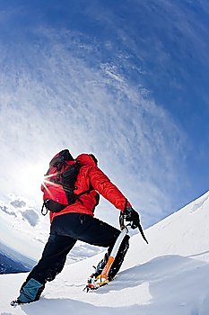Mountaineer reaching the top of a snowcapped mountain peak. Vertical frame.