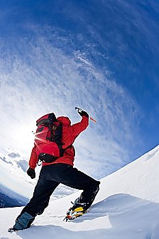 Mountaineer reaching the top of a snowcapped mountain peak. Vertical frame.