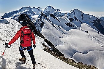 Mountaineer walks down along the snowy ridge of Breithorn, exactly on the swiss-italian border. IIn background the main peaks of Monte Rosa massif (4650 mt, the second highest point in continental Europe) Switzerland, Europe.