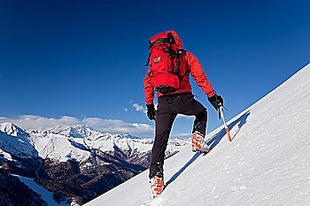 A male climber , dressed in red, climbs down a snowy slope. Winter clear sky day. In background the Monte Rosa massif, Italy, Europe.