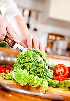 Woman´s hands cutting lettuce, behind fresh vegetables.
