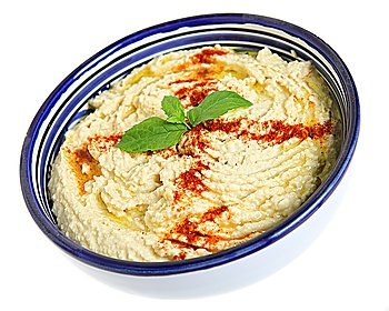 Hummus chickpea dip garnished with paprika and basil in a Tunisian-made pottery bowl with a typical blue and white pattern.
