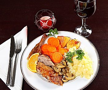 A candle-lit dinner of roast duck, potatoes, carrots and mushrooms with wine.