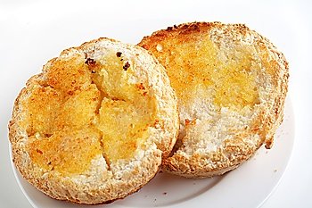 A gluten-free roll that has been halved, toasted and buttered, on a white plate