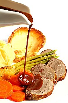 A meal of roast beef with carrots, Yorkshire puddings, potatoes and asparagus, with gravy being poured on