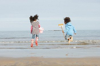 Two Children Playing By Sea On Winter Beach