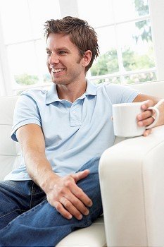 Man Sitting On Sofa Drinking Coffee Relaxing At Home