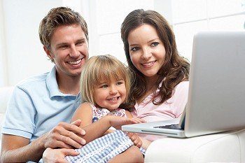 Family Sitting On Sofa Using Laptop At Home