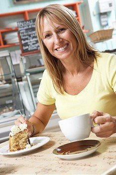 Female Customer Enjoying Slice Of Cake And Coffee In Cafe 