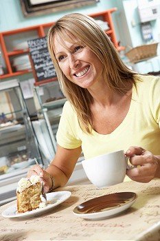 Female Customer Enjoying Slice Of Cake And Coffee In Cafe 