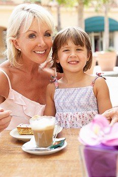 Grandmother With Granddaughter Enjoying Coffee And Cake In CafZ