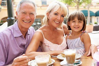 Grandparents With Granddaughter Enjoying Coffee And Cake In CafZ