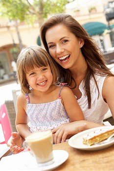 Mother And Daughter Enjoying Cup Of Coffee And Piece Of Cake In CafZ