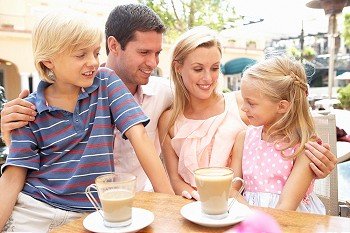 Young Family Enjoying Cup Of Coffee In CafZ Together