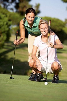 Two Female Golfers On Golf Course Lining Up Putt On Green