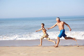 Grandfather chasing young boy on beach