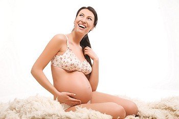 Happy pregnant female sitting on carpet