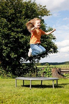 Little girl on a trampoline in a garden, in the background a fence and some landscape