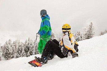 Skier and snowboarder sitting in the snow looking into an alpine winter landscape