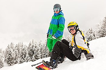 Skier and snowboarder sitting in the snow looking into an alpine winter landscape