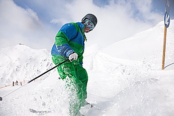 Man on a ski track going downhill, stopping in front of camera dusting some snow 