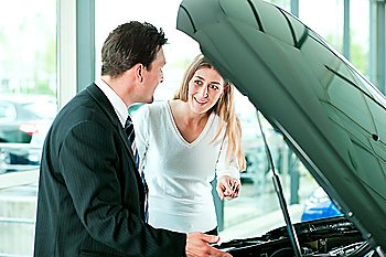 Woman buying a car in dealership looking under the hood at the engine