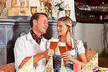 Couple in Bavarian Tracht drinking wheat beer in a typical pub, clinking glasses