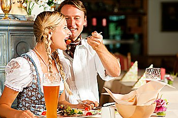 Couple in Bavarian restaurant, wearing Tracht eating Wurstsalat and having wheat beer glasses in the table