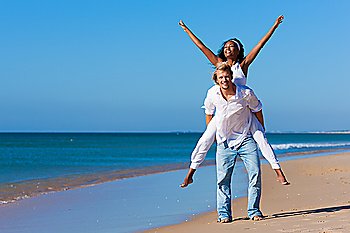 Couple in love - Caucasian man having his African-American woman piggyback on his back under a blue sky on a beach