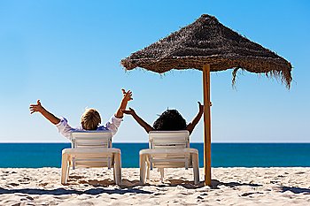 Couple sitting in sun chairs under an parasol sunshade on a beach stretching arms, feeling free