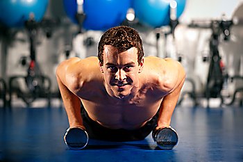 Very strong and muscular man exercising by doing pushups in a gym