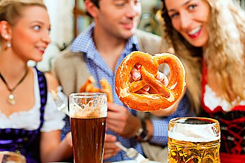 Inn or pub in Bavaria - group of young men and women in traditional Tracht drinking beer and eating pretzel