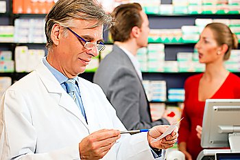Pharmacist with customers in pharmacy, he is holding a prescription slip in his hands