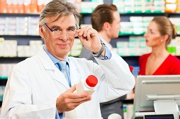 Pharmacist with customers in pharmacy, he is holding a prescription slip in his hands